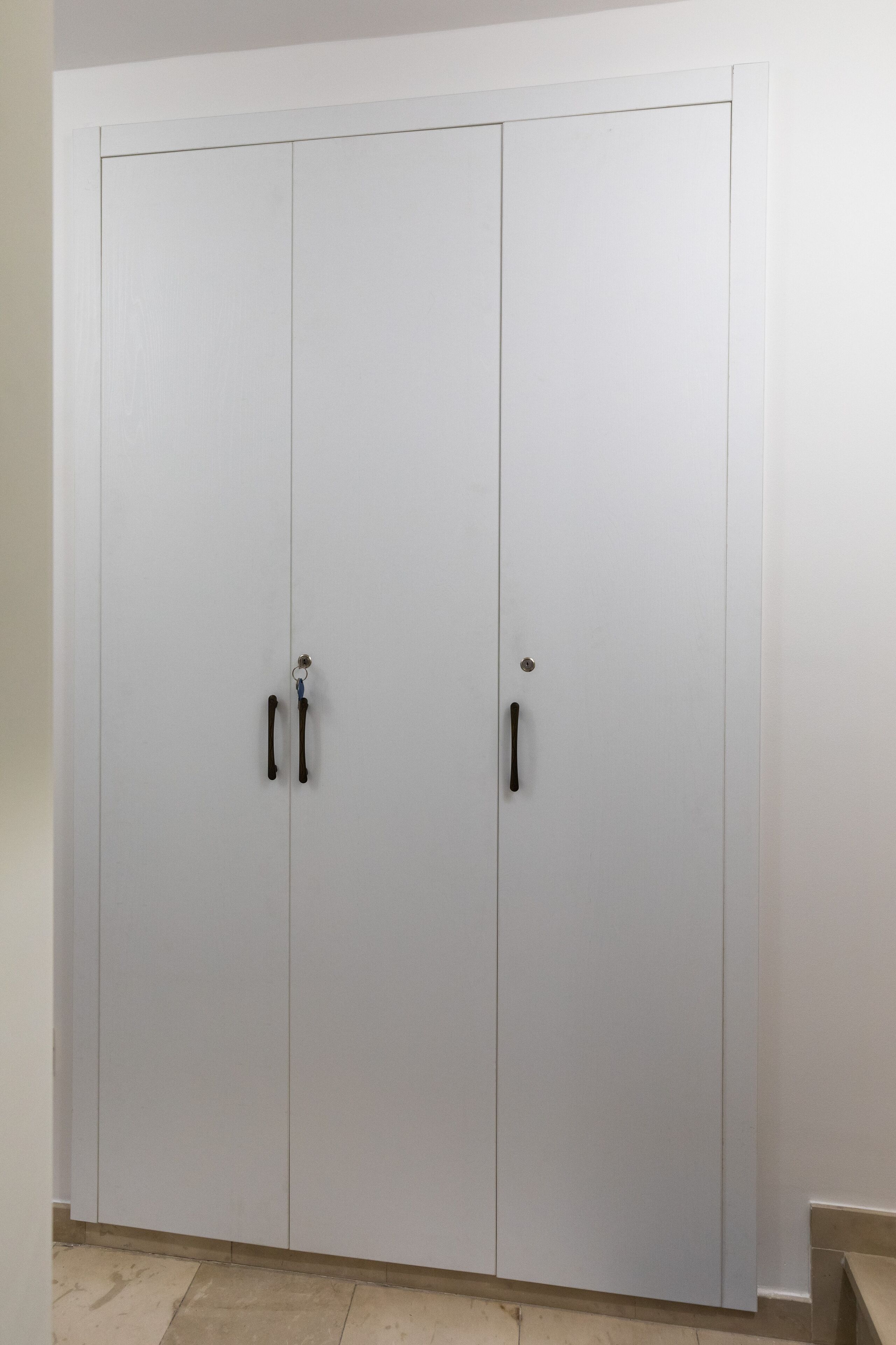 Un armario blanco con dos puertas y un tirador en cada una.