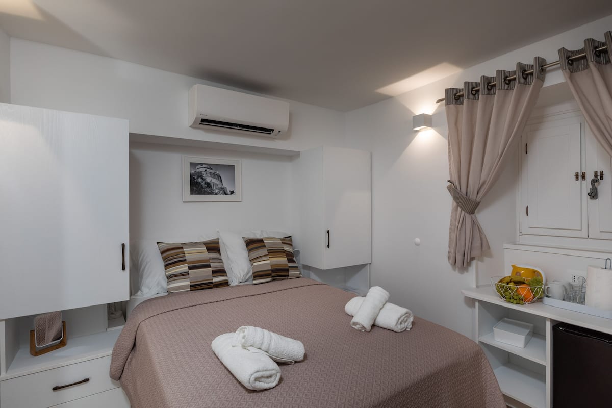 Een verzorgde slaapkamer met een bed, kussens, een nachtkastje met een fruitschaal en een spiegel.