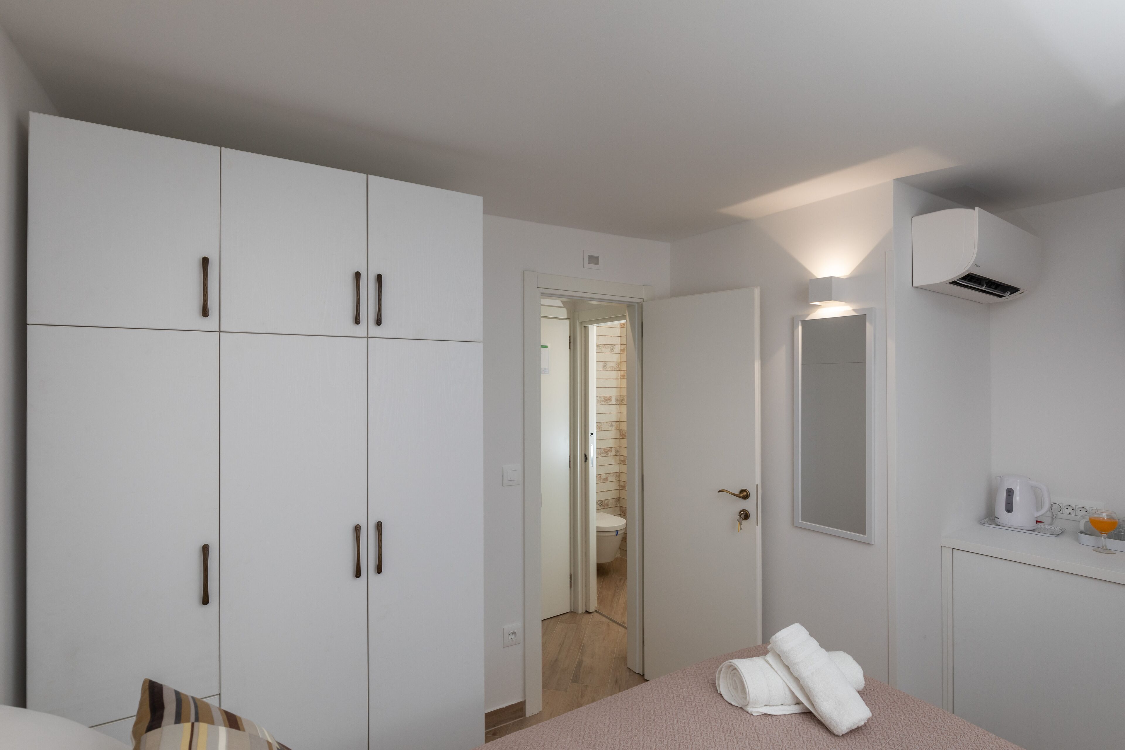 A bedroom with a bed, a wardrobe, a mirror, and a bedside table with a kettle and glasses.