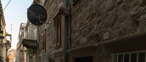A narrow street with stone buildings, a visible door with a sign, and a satellite dish.