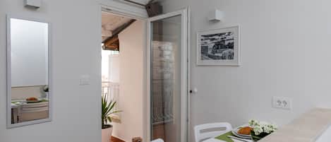 A dining area with a table set for two, a potted plant, and a framed picture on the wall.