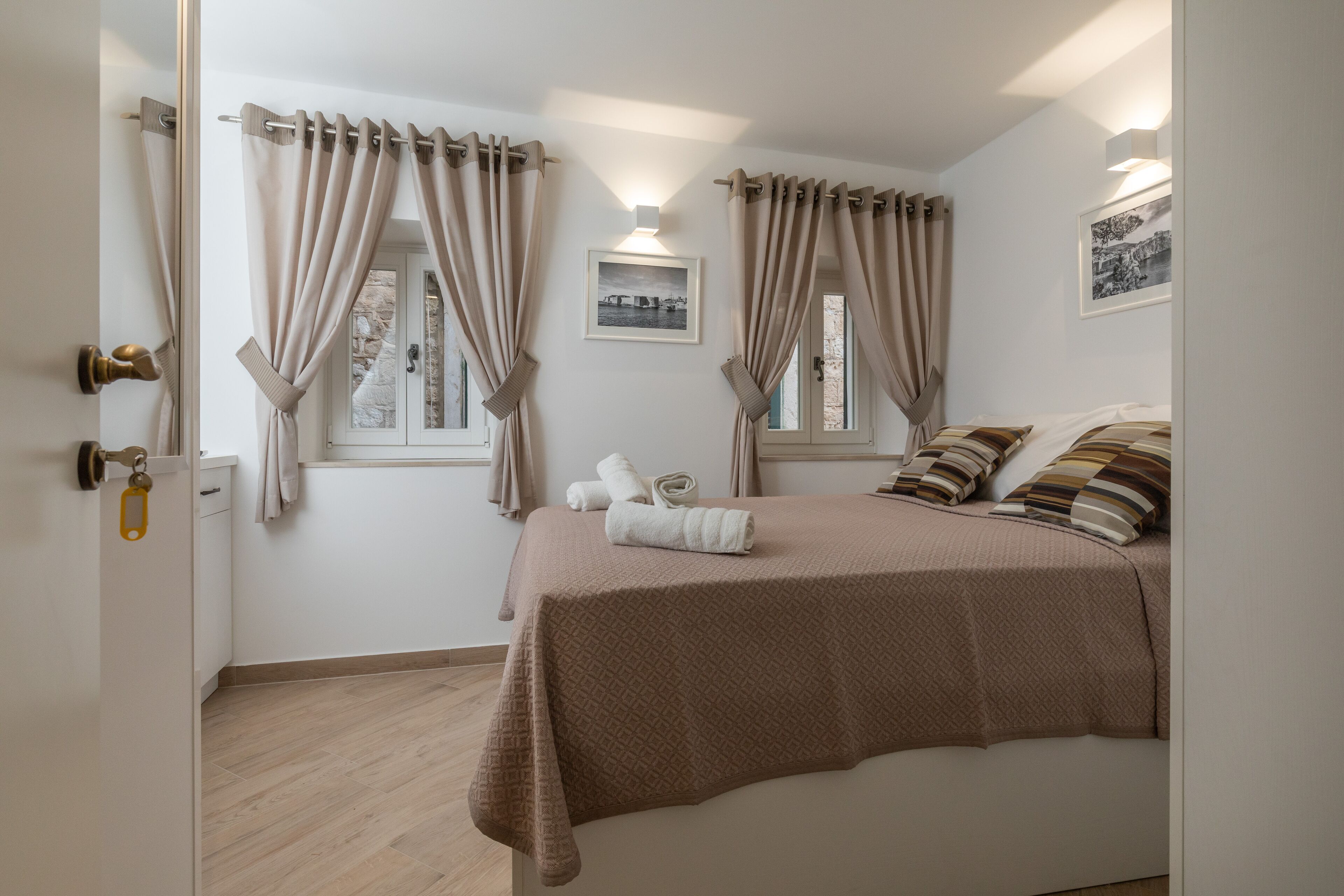 A bedroom with a bed, curtains, a window, a picture on the wall, and a door with a lock.