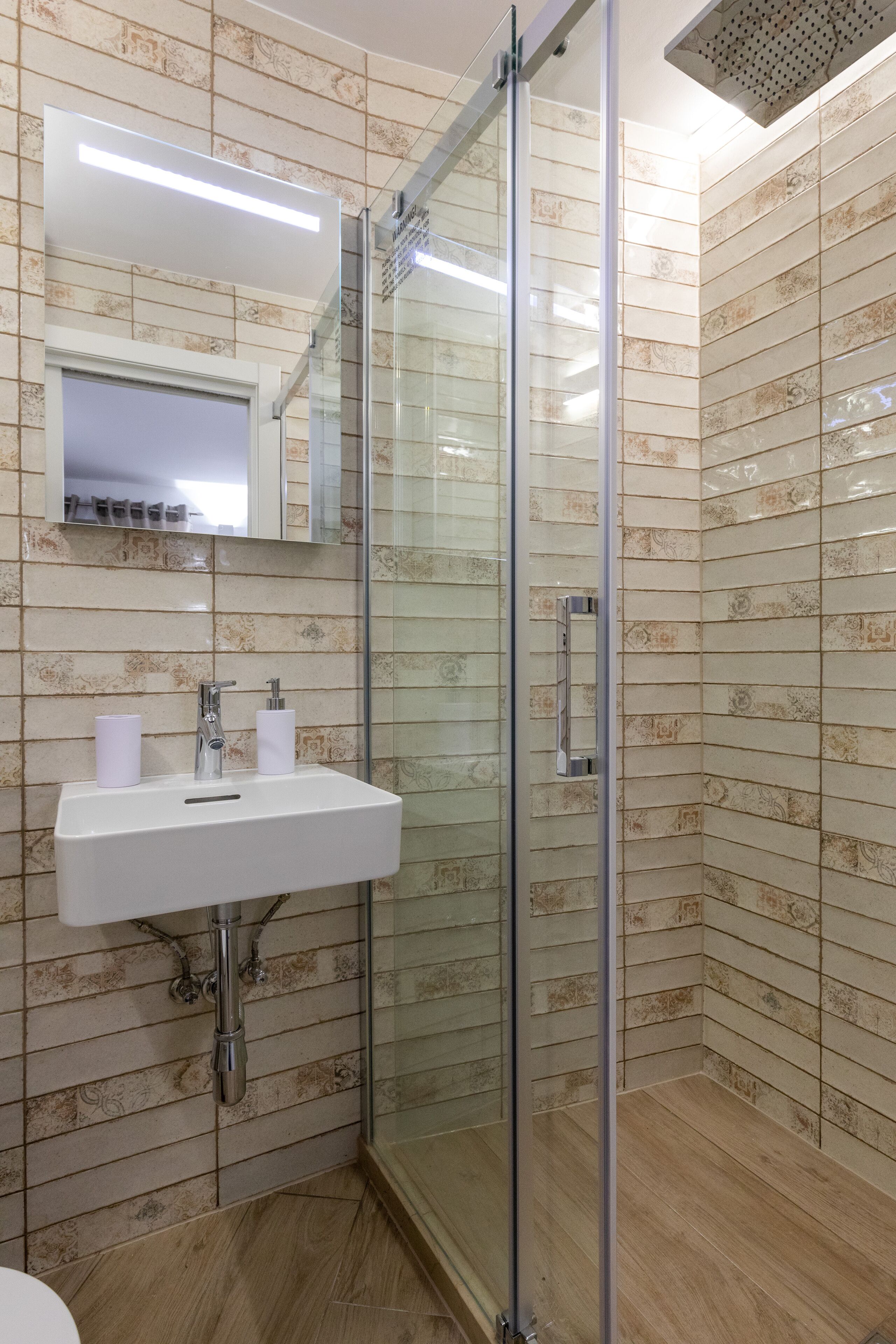A modern bathroom with a glass-enclosed shower, a white sink, and a mirror above it.
