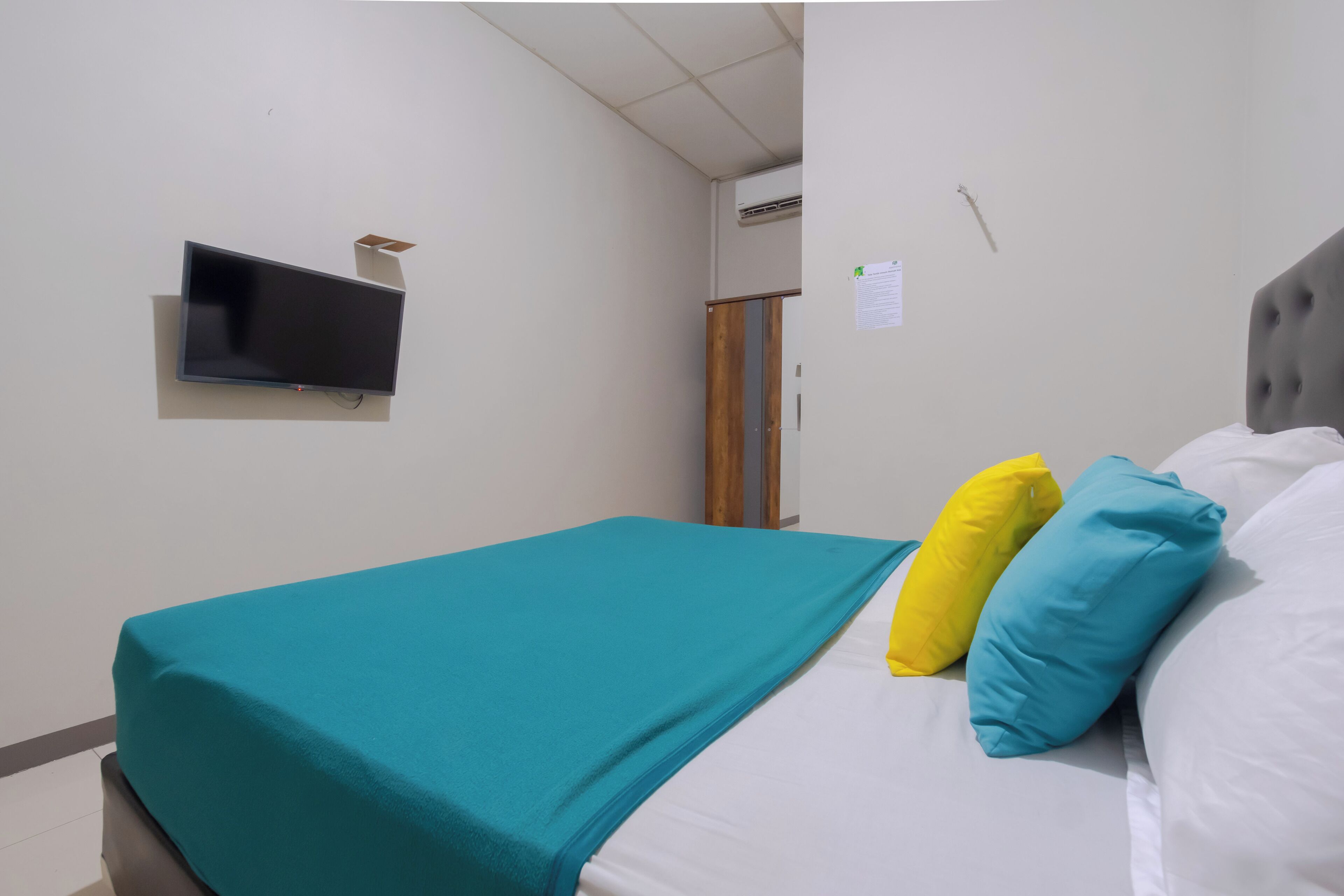 Quarto com cama, televisão de tela plana na parede e uma porta.