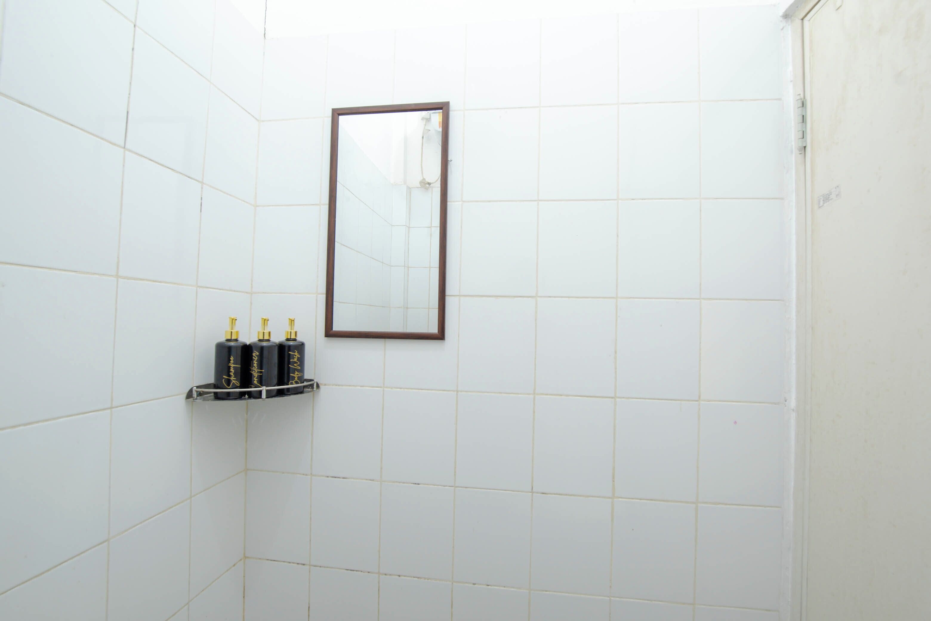 Une salle de bain avec des murs carrelés de carreaux blancs, un miroir et une étagère contenant des articles de toilette.