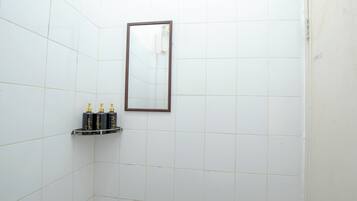 A bathroom with white tiled walls, a mirror, and a shelf with toiletries.