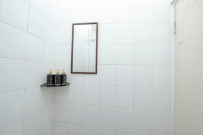 A bathroom with white tiled walls, a mirror, and a shelf with toiletries. - Athena Syariah Residence (Tangerang)