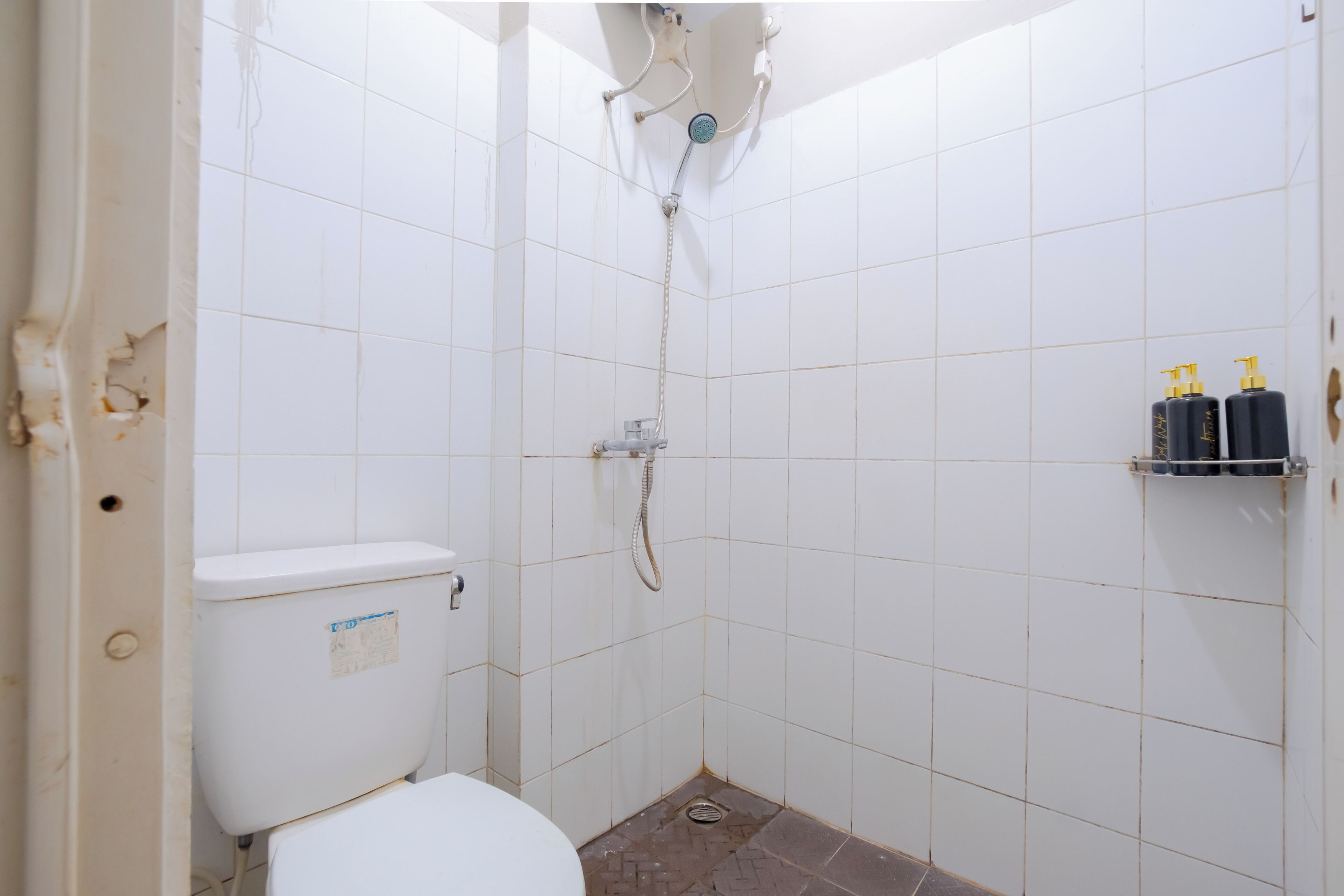 Een kleine badkamer met tegels, een toilet, douche en een plank met toiletartikelen.