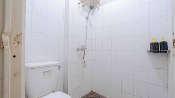 Een kleine badkamer met tegels, een toilet, douche en een plank met toiletartikelen.
