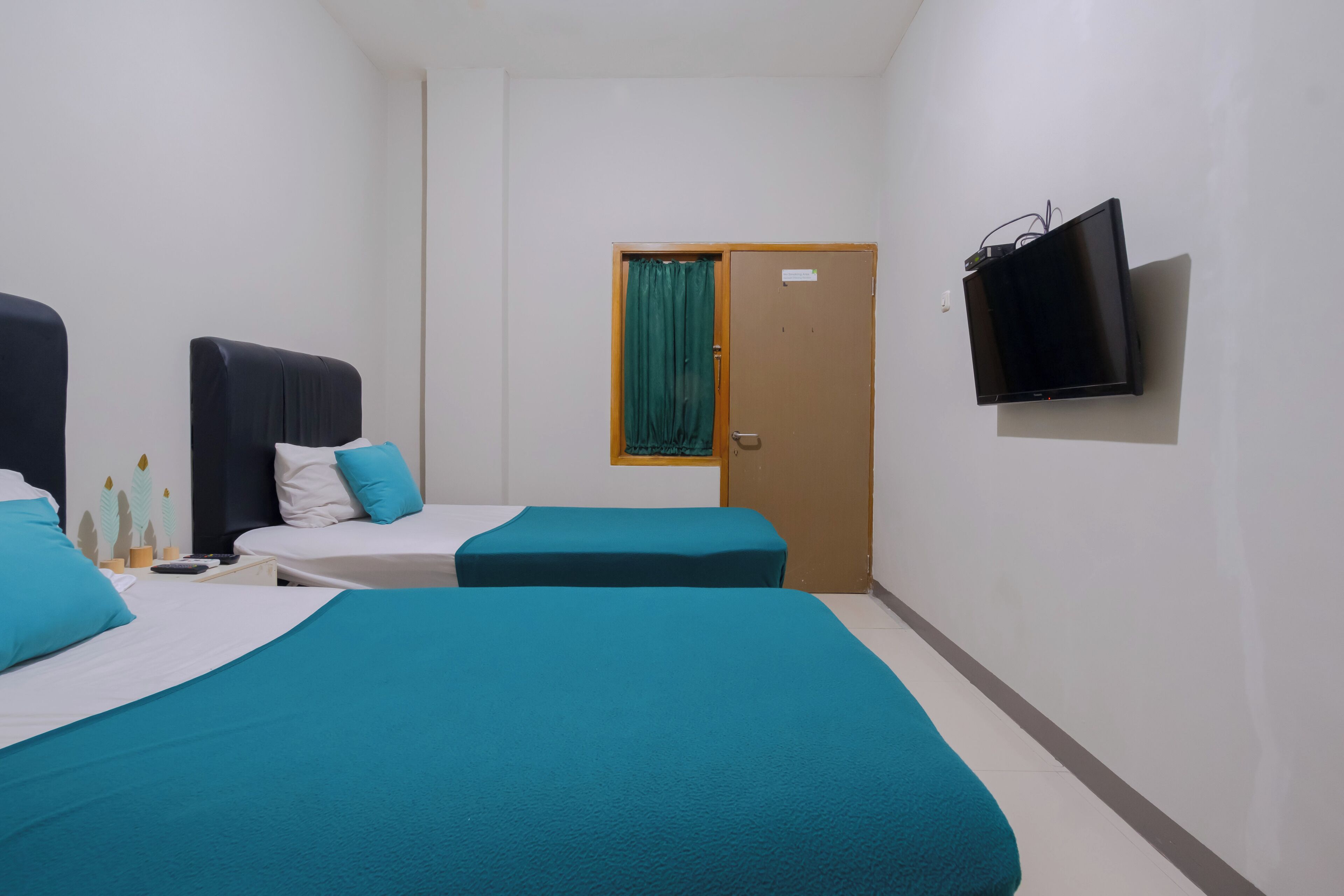 A hotel room with two beds, a television, and a door with a curtain.