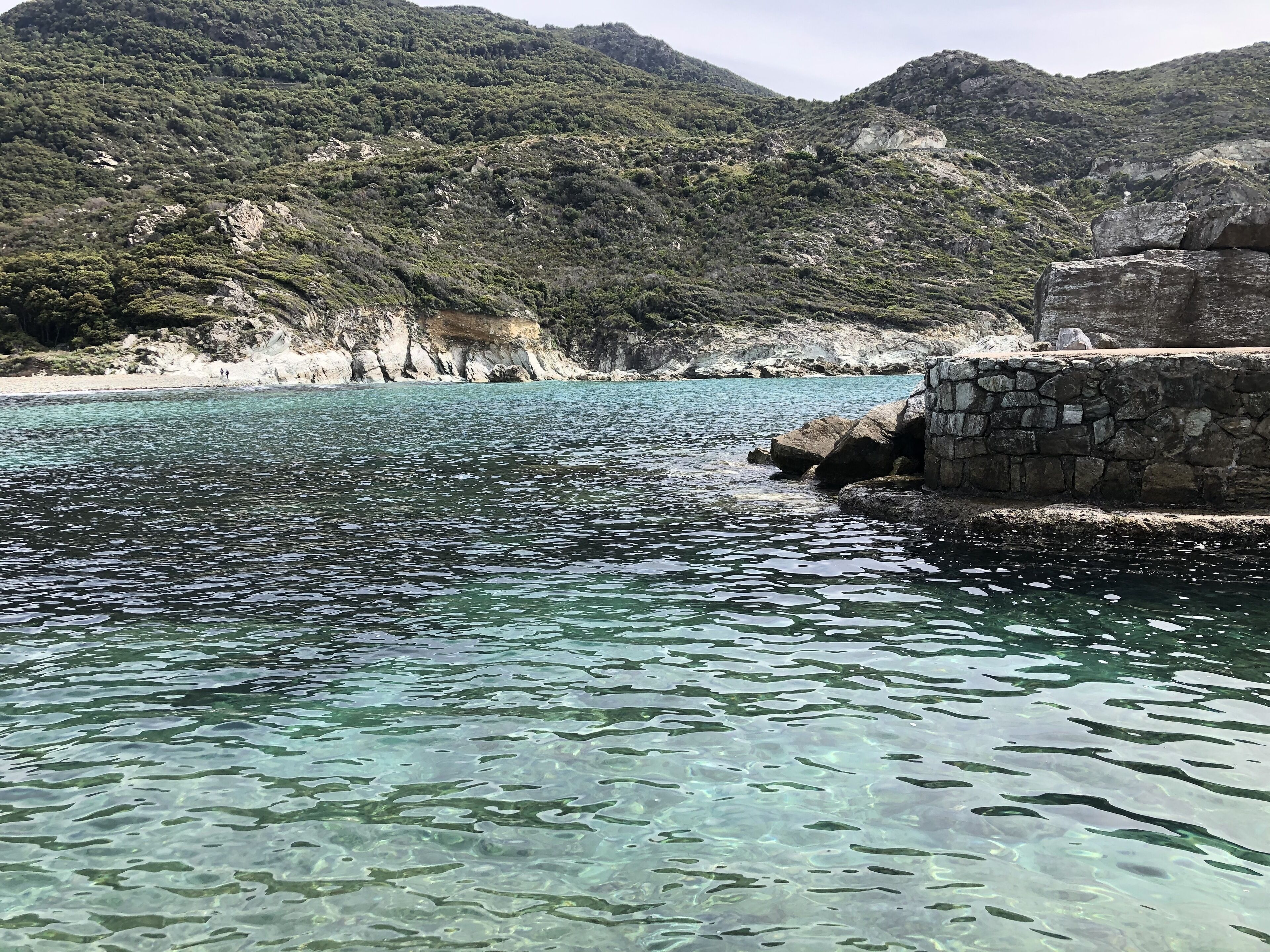 A coastal area with clear water, rocky terrain, and a stone wall.