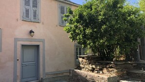 Ein Geb äude mit geschlossenem Fensterladen und einer Holztür, eine Steinmauer und ein Baum im Hintergrund.