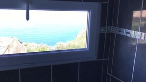Ein Badezimmer mit dunklen Fliesen, einem Fenster mit Meerblick und einer kleinen Ablagefläche.