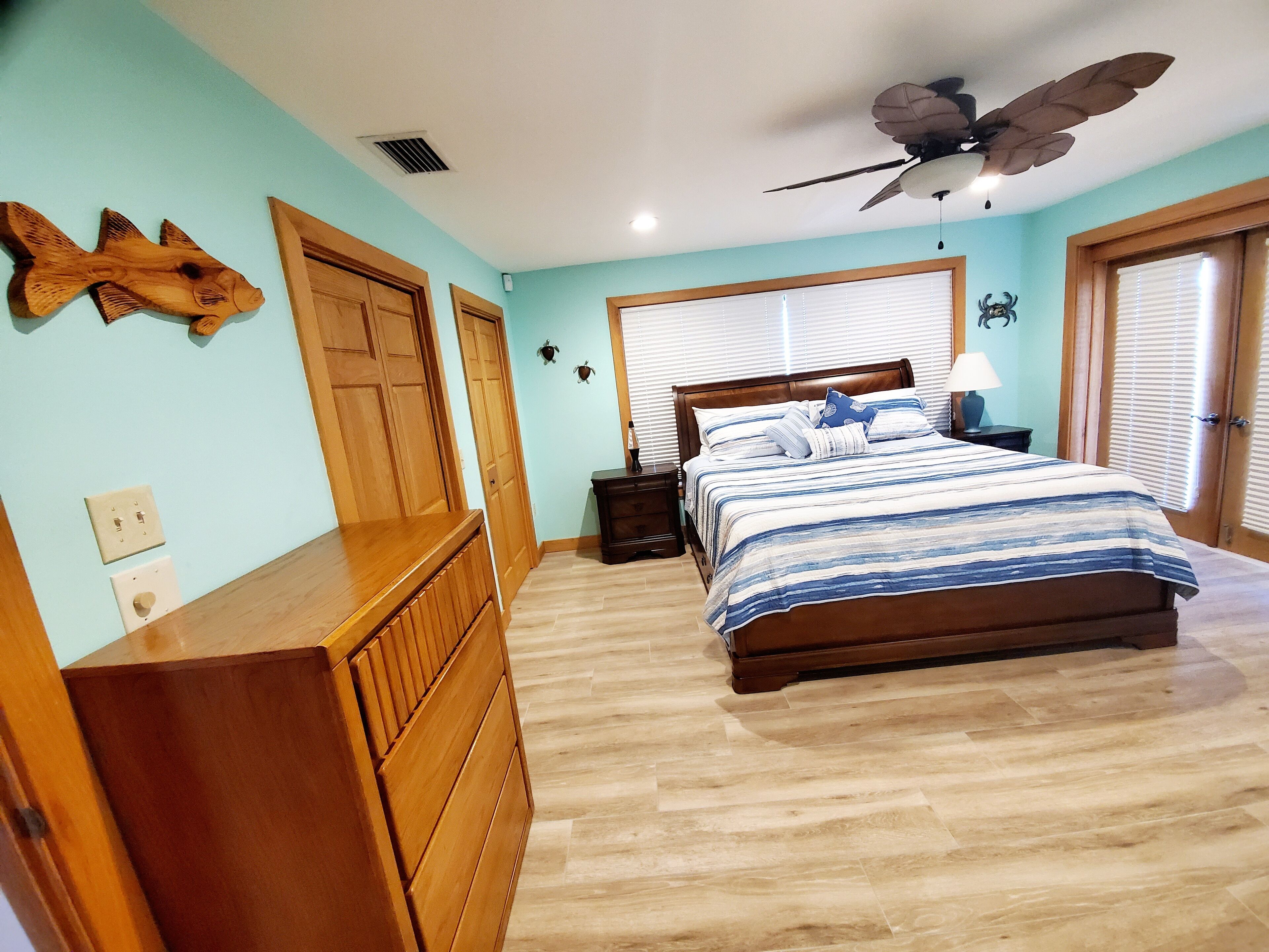 Een slaapkamer met een bed, een houten dressoir, een plafondventilator en wandlampen.