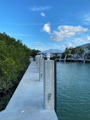 A waterfront walkway with concrete pillars, a clear sky, and a calm water body.