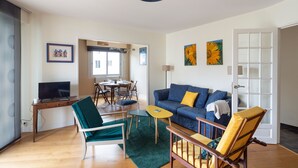 Un salon comprenant un canapé, des fauteuils, une table basse, un téléviseur posé sur un bureau et des œuvres d’art accrochées aux murs.