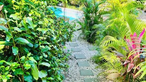 A garden pathway leading to a pool area surrounded by lush greenery and a stone-tiled deck. - 3 min walking distance to Nosara beach (Guanacaste)