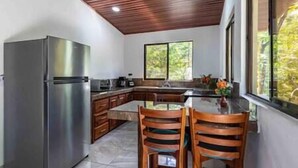 A kitchen with a stainless steel refrigerator, wooden cabinets, a glass dining table, and two wooden chairs. - 3 min walking distance to Nosara beach (Guanacaste)