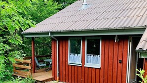 A red wooden cabin with a metal roof, a small porch, and a door with a glass panel.