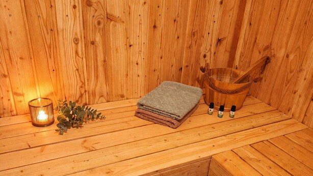 A wooden sauna bench with a towel, a candle, and essential oils.