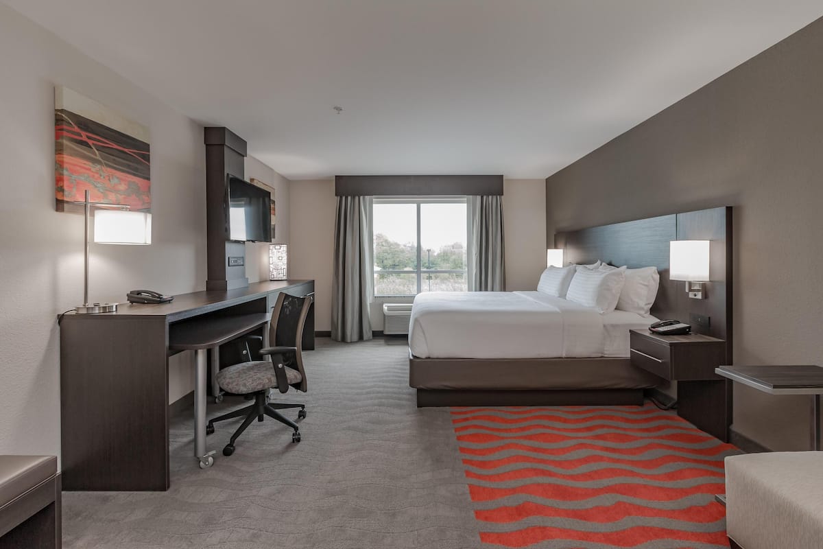A hotel room with a bed, desk, chair, and a view of the outdoors.