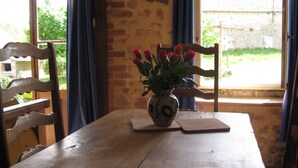 Una mesa de madera con un jarrón de rosas rojas, dos posavasos de madera y un muro de ladrillo al fondo.