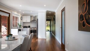 Una cocina moderna con armarios blancos, una campana extractora de acero inoxidable y un comedor con una mesa y sillas blancas.