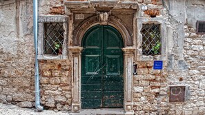 Edifici històric amb una porta doble verda, parets de pedra i una petita finestra amb reixatge metàl·lic.