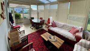 A sunroom with a dining table, chairs, a sofa, and a patterned rug. - Beachfront at Baie des Trépassés (Cléden-Cap-Sizun)