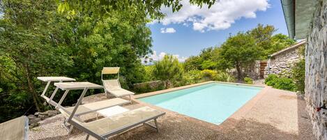 A pool area with a rectangular pool, two lounge chairs, and a table.