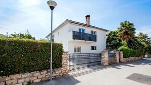 Une maison à deux étages, avec une façade blanche, un balcon noir et un mur en pierre.
