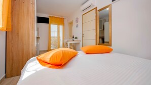 Une chambre à coucher avec un lit, deux oreillers orange, une table de chevet avec une bouteille et un verre, et un miroir sur le mur.
