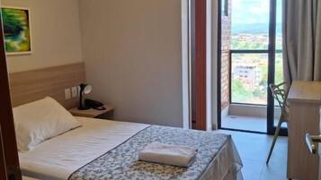 Habitación de hotel con cama, escritorio, silla, aire acondicionado y vistas al exterior.