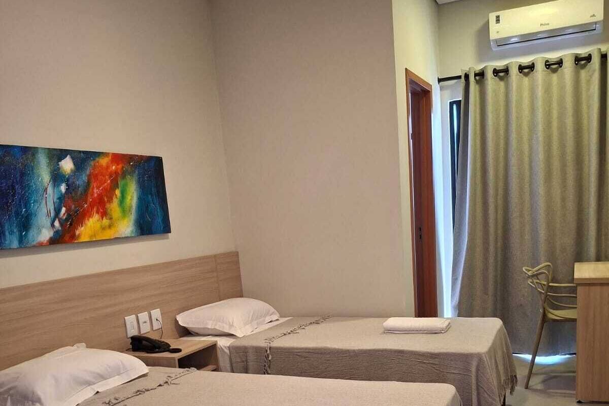 Habitación de hotel con dos camas, un escritorio, una silla, un cuadro en la pared y un equipo de aire acondicionado.