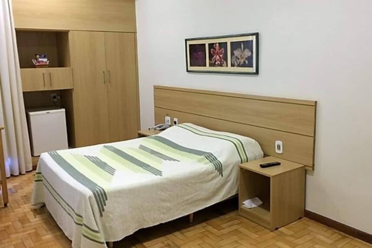 Un dormitorio con cama, mesita de noche, armario y un pequeño refrigerador.