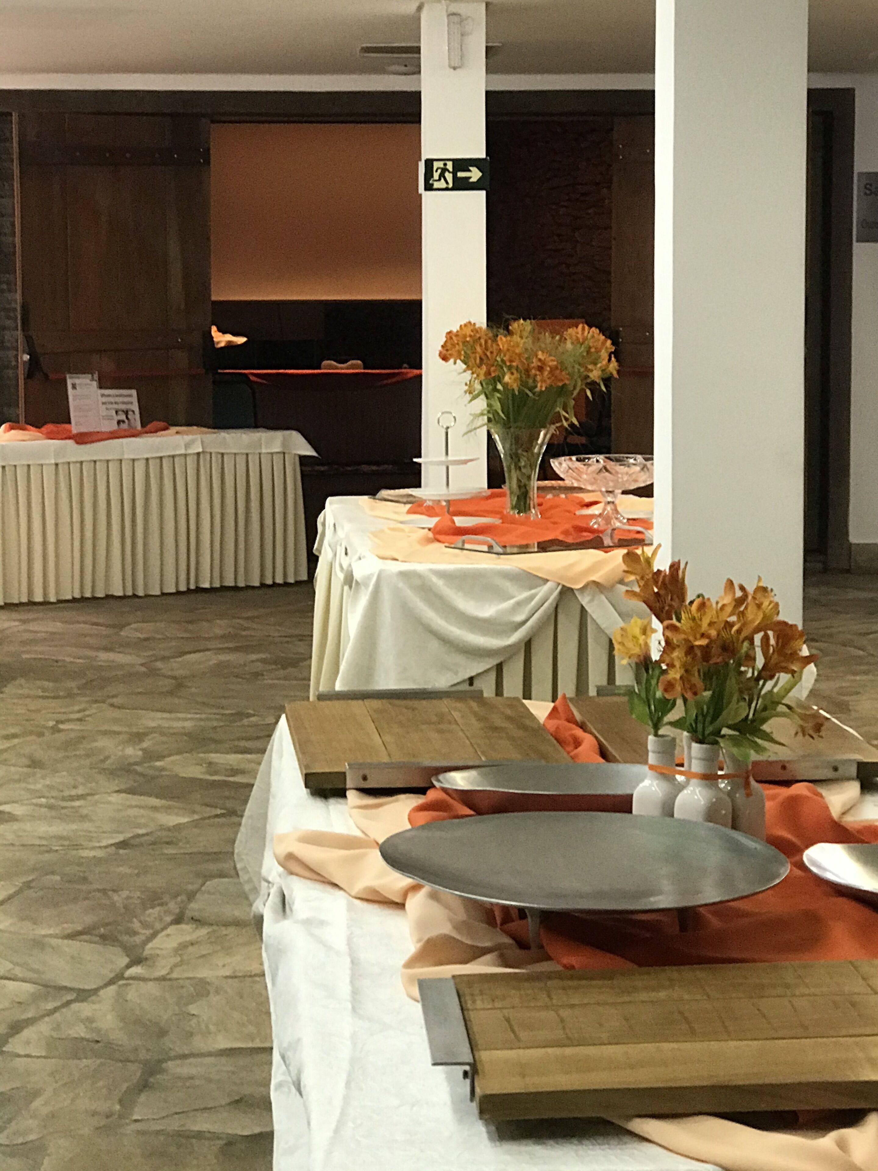 Ein Konferenzraum mit für eine Veranstaltung gedeckten Tischen, mit weißen Tischdecken, orangefarbenen Servietten und Blumenarrangements.