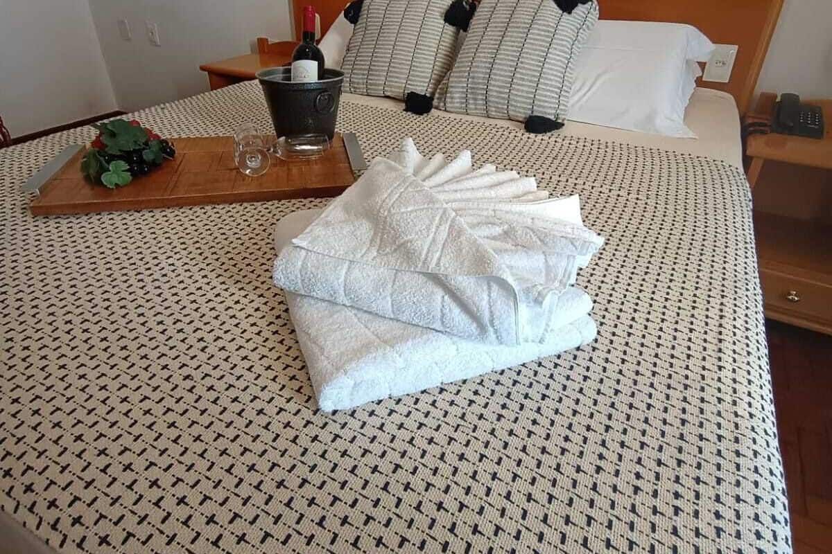 Una cama bien hecha con una colcha estampada, una bandeja de madera con una botella y uvas, y un cuadro con flores en la pared.