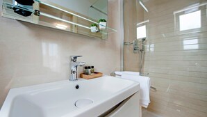 A modern bathroom with a large white sink, a glass shelf with toiletries, a glass shower enclosure, and a mirror above the sink. - TEREZA GOLD - Studio Apartment (Rovinj)