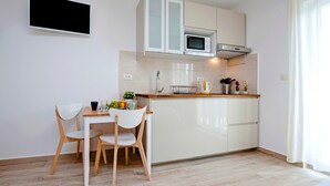 A modern kitchen with white cabinets, a microwave, and a sink. There is a dining table with two chairs and a fruit bowl. - TEREZA GOLD - Studio Apartment (Rovinj)