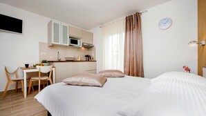 A hotel room with a bed, a desk with a chair, a kitchenette, and a clock on the wall. - TEREZA GOLD - Studio Apartment (Rovinj)
