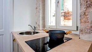 Una cocina con un lavamanos de acero inoxidable, una placa de inducción negra y una olla con asas de madera.