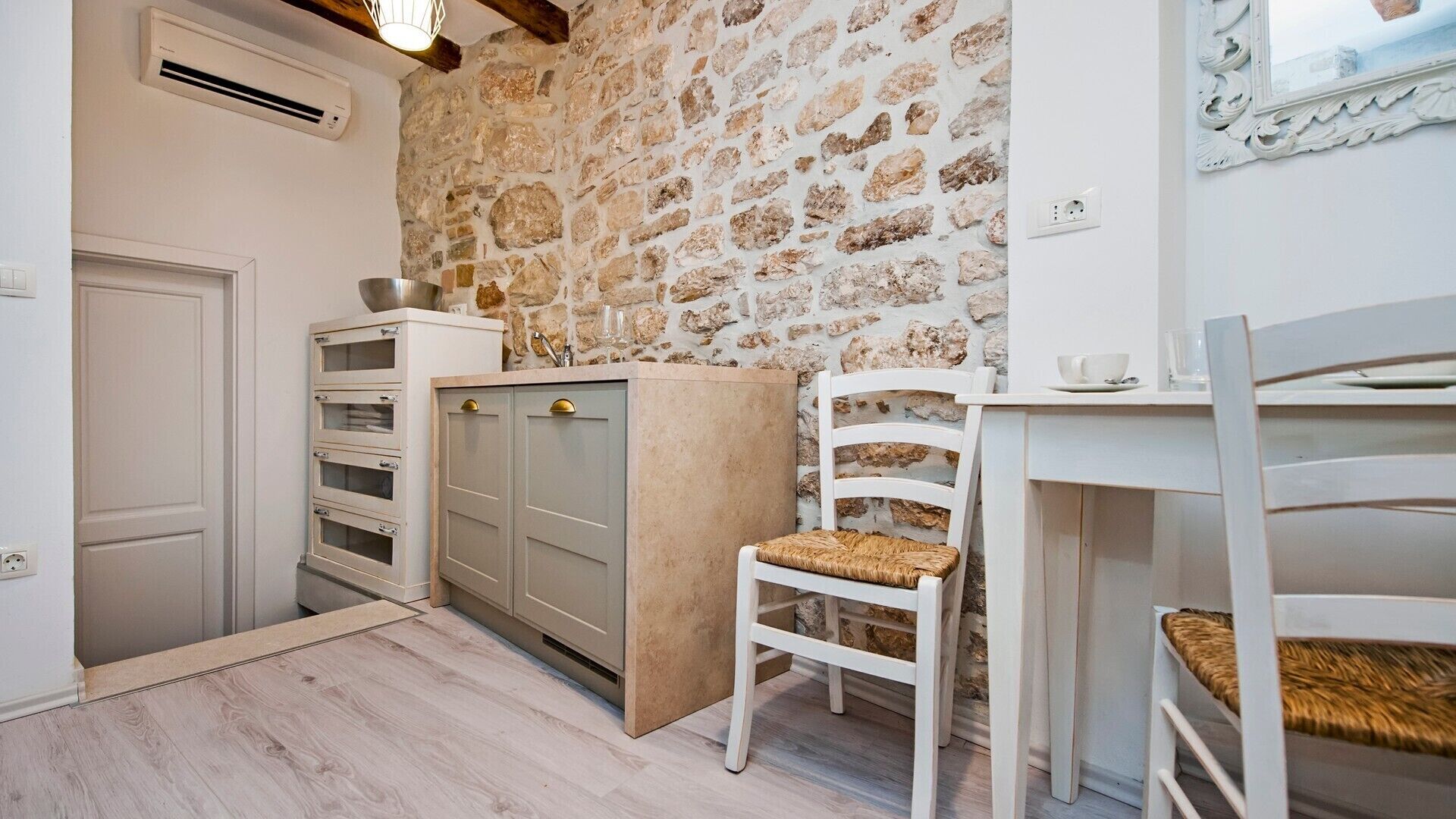 A compact kitchen with stone wall backsplash, white cabinetry, and a wooden floor.