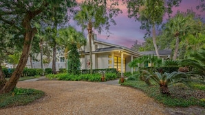 A building with a gravel driveway, surrounded by lush greenery and palm trees. - Beautiful East Beach Cottage with Pool (St. Simons)
