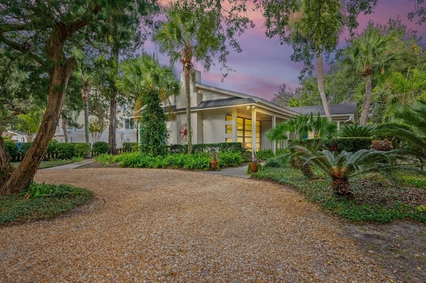 A building with a gravel driveway, surrounded by lush greenery and palm trees.
