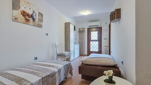 Een compacte hotelkamer met twee enkele bedden, een klein tafeltje met een vaas, een stoel, een kledingkast en een deur met een raam.