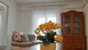 Een woonkamer met een bank, een gele vaas met bloemen en een houten kast.