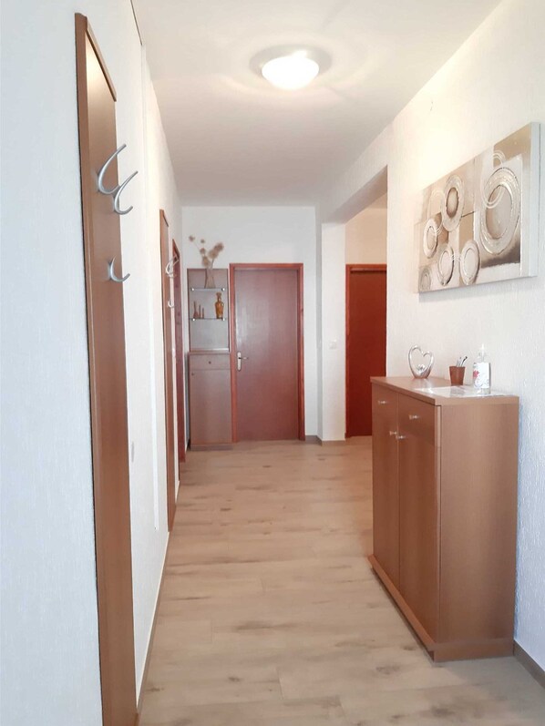 A hallway with wooden flooring, a wooden cabinet with a mirror, and a door with a small shelf above it. - MONTE GRANDE - Three Bedroom Apartment (Pula)