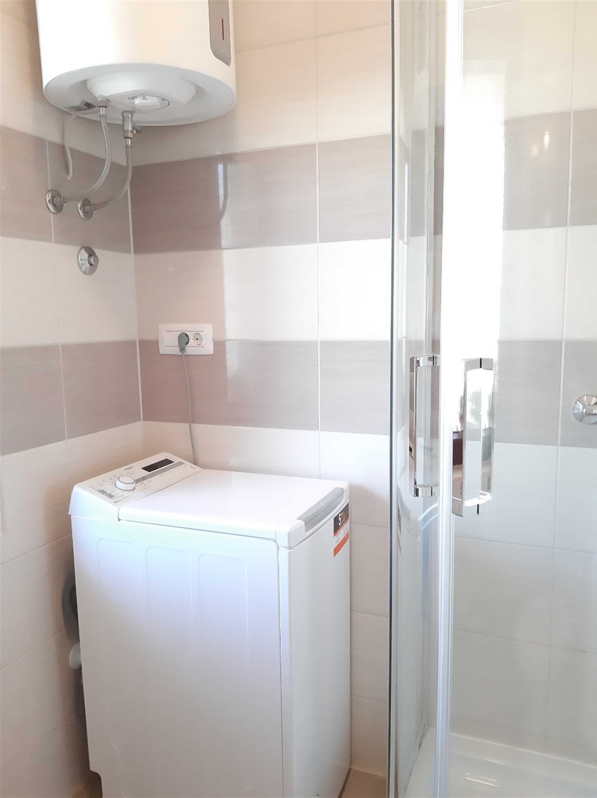 A compact bathroom with a glass shower enclosure, a white washing machine, and a wall-mounted sink.
