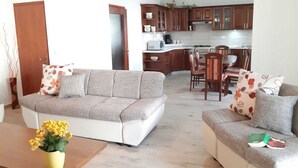 Een woonkamer met een bank, een salontafel met een bloevas, en een eethoek met stoelen en een tafel.