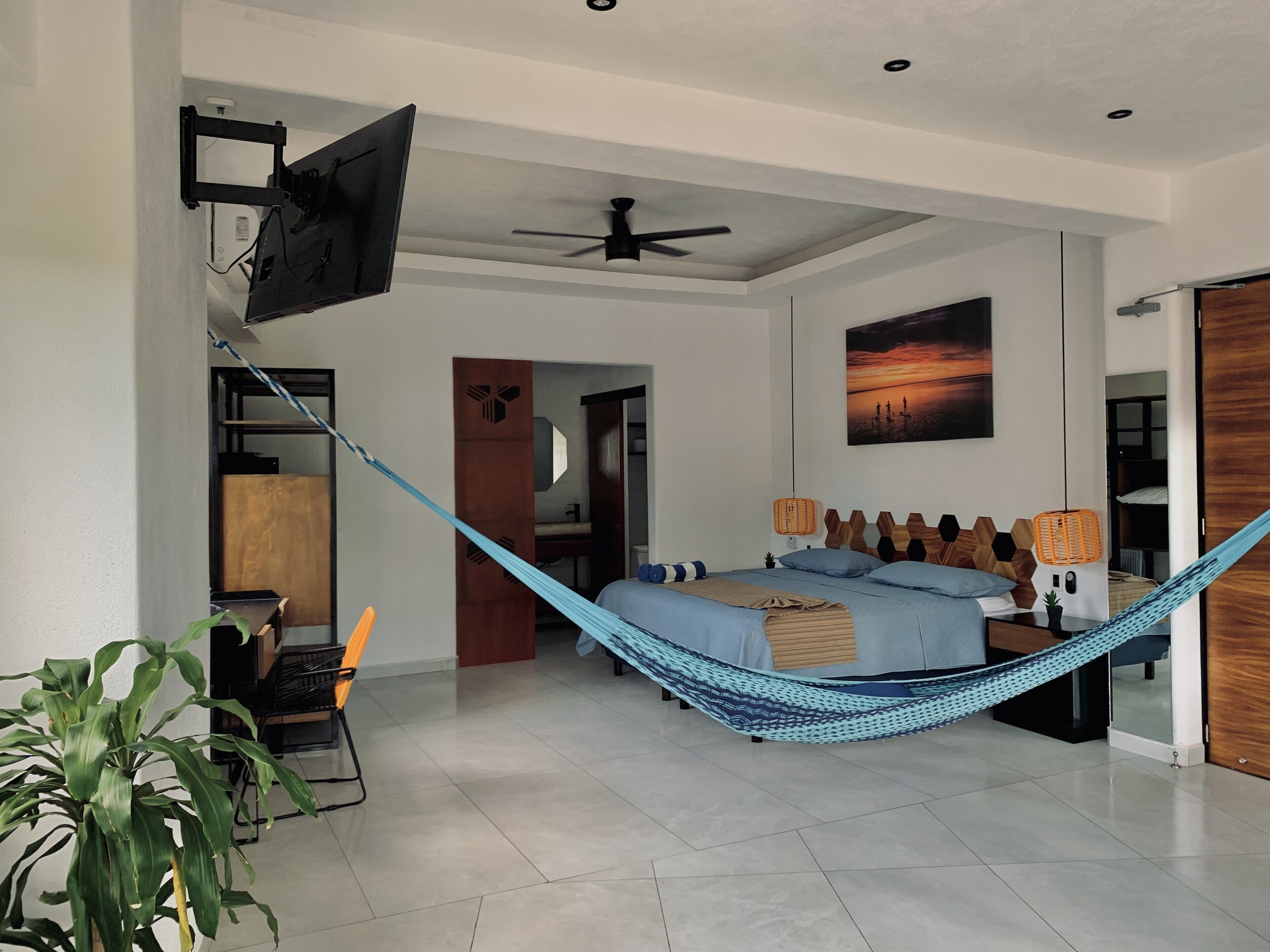 A modern bedroom with a bed, a hammock, a ceiling fan, and a wall-mounted TV.